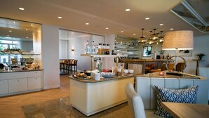 A modern kitchen with a central island, bar area, seating, and a dining area. - Hotel Engbert (Oelde)