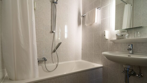 A modern bathroom with a bathtub, a sink, and a mirror. - Hotel Engbert (Oelde)