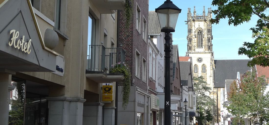 Un hotel con un cartel, una farola y una iglesia al fondo.