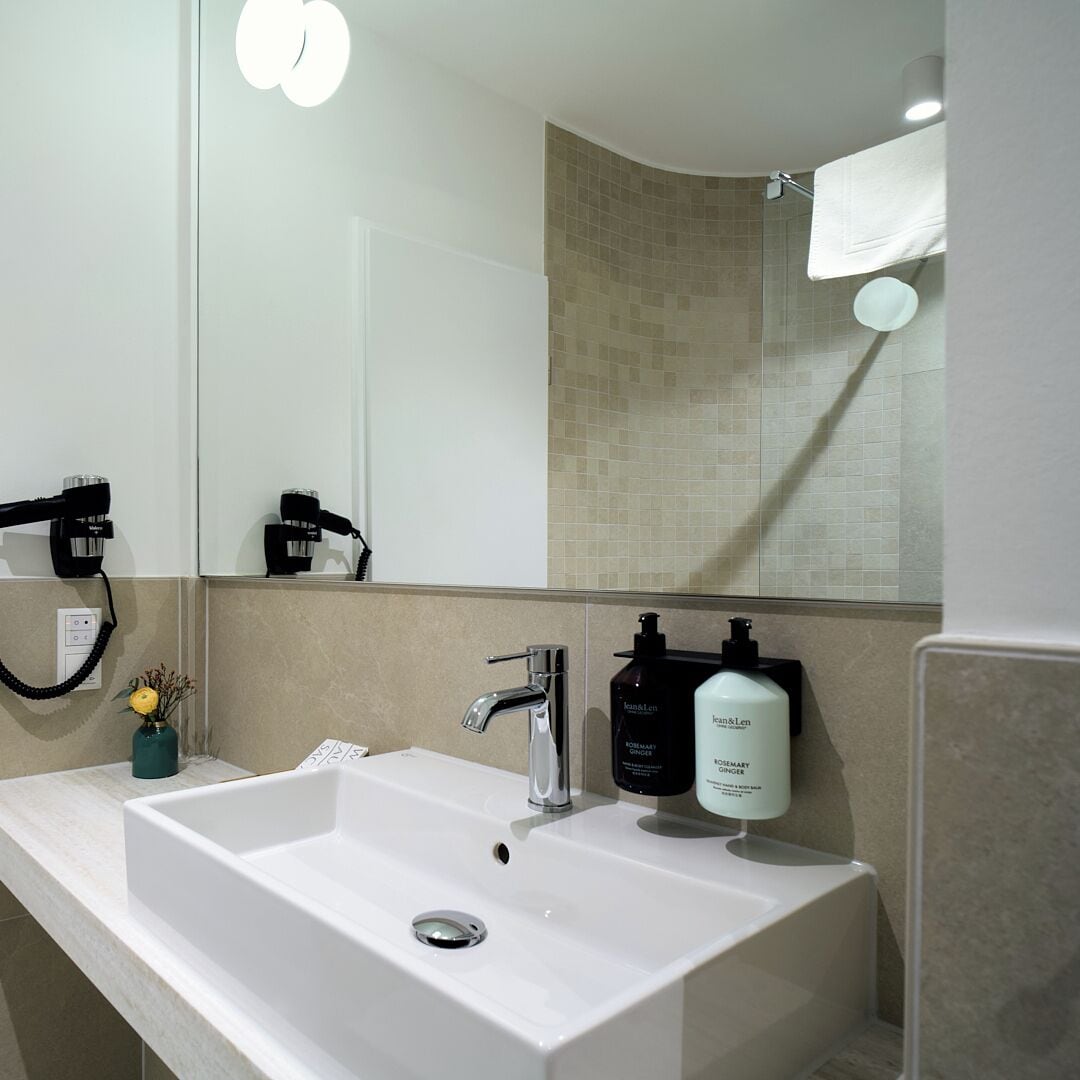 Un baño moderno con un lavamanos blanco, un espejo y un perchero para toallas.