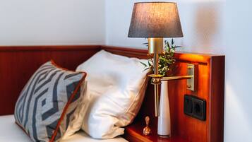 En snyggt bäddad säng med en mönstrad kudde och en lampa på ett litet bord i trä som står vid sängen.