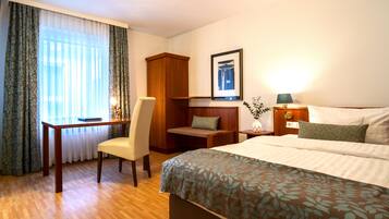 Een hotelkamer met een bed, bureau, stoel, garderobe en nachtkastje met lamp.