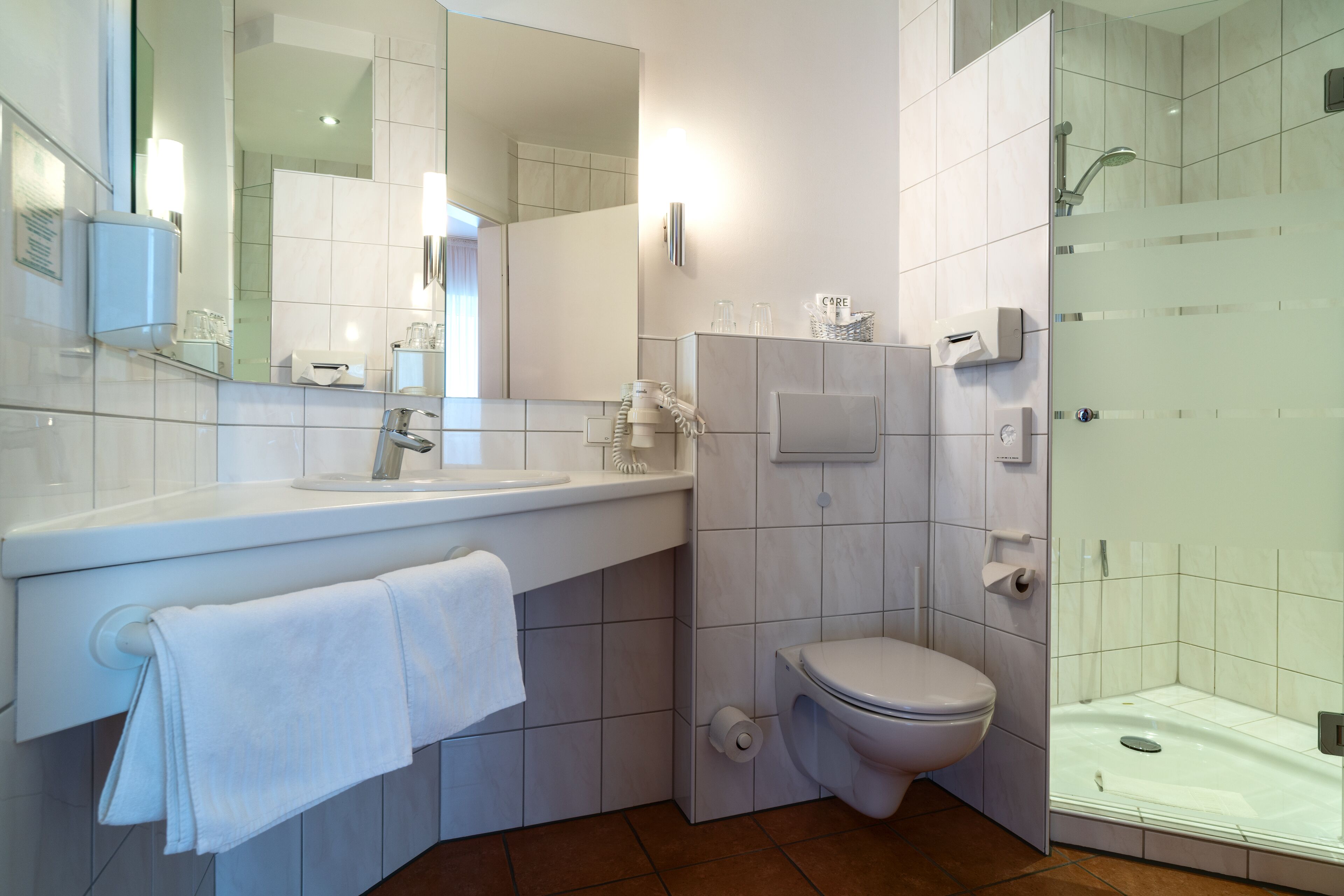 Un baño moderno con un lavamanos, espejo y retrete blancos.