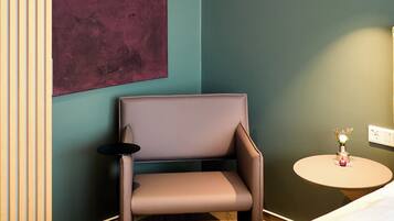 A modern room with a brown chair, a small round table with a vase, and a large abstract painting on the wall.