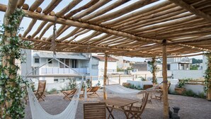 An outdoor patio with wooden furniture, including a hammock and a table, set on a gravel surface.