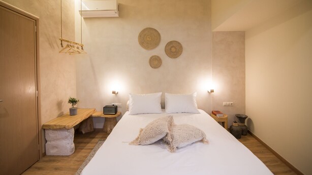 A bedroom with a bed, bedside tables, a nightstand, an air conditioner, and wall decor.