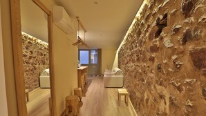 A hallway with a stone wall, wooden furniture, and a view into another room.
