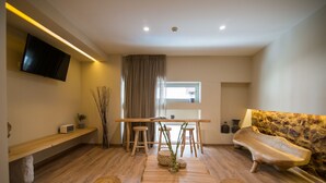 A modern living room with a wooden table, two stools, a sofa, and a TV mounted on the wall.