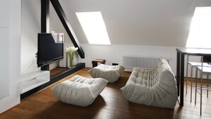 Ein modernes Loft mit schrägverdachter Decke, einem an der Wand montierten Flachbildfernseher und einem Essbereich mit Tisch und Stühlen.