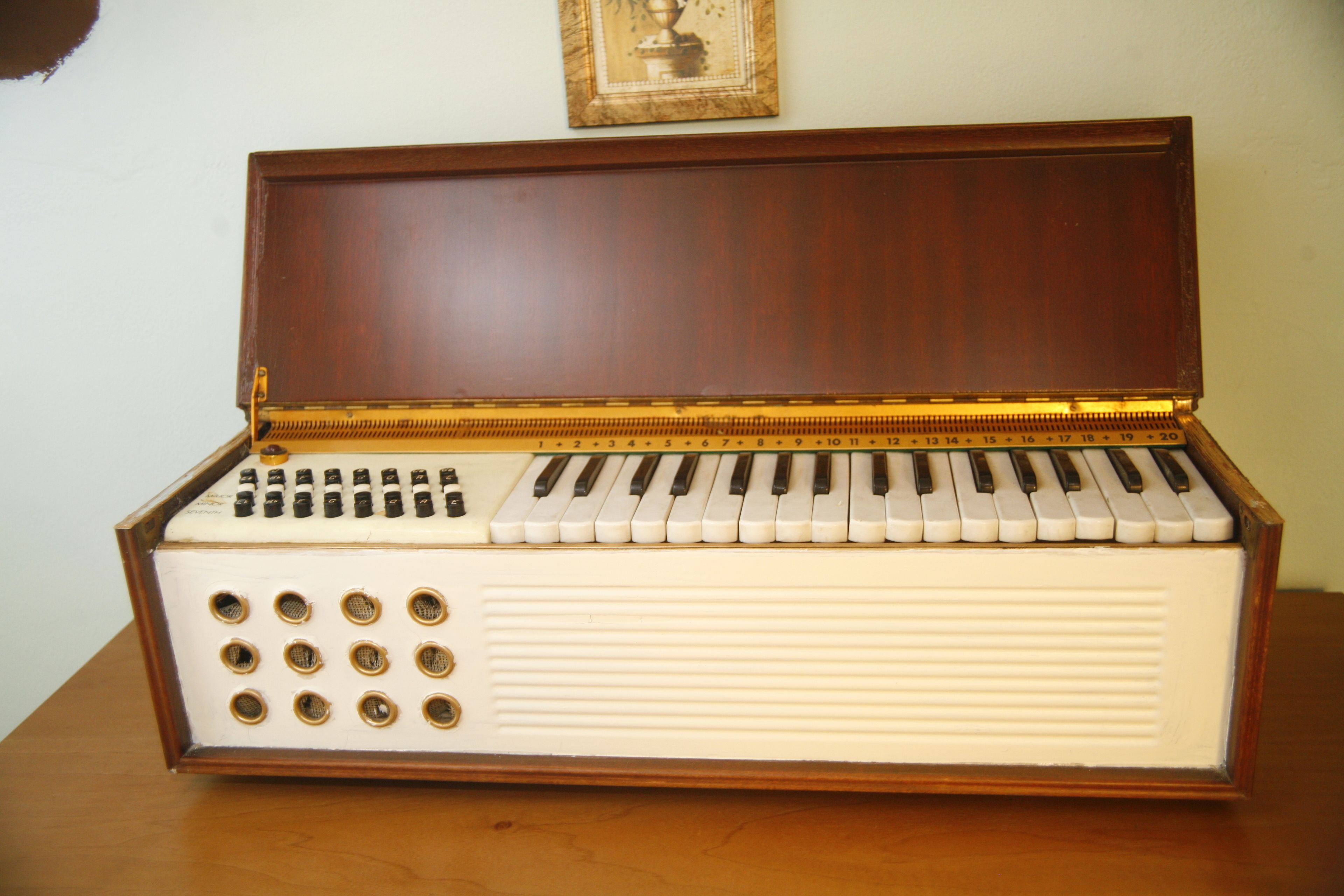An upright piano with a wooden finish and a white body, placed on a wooden surface.