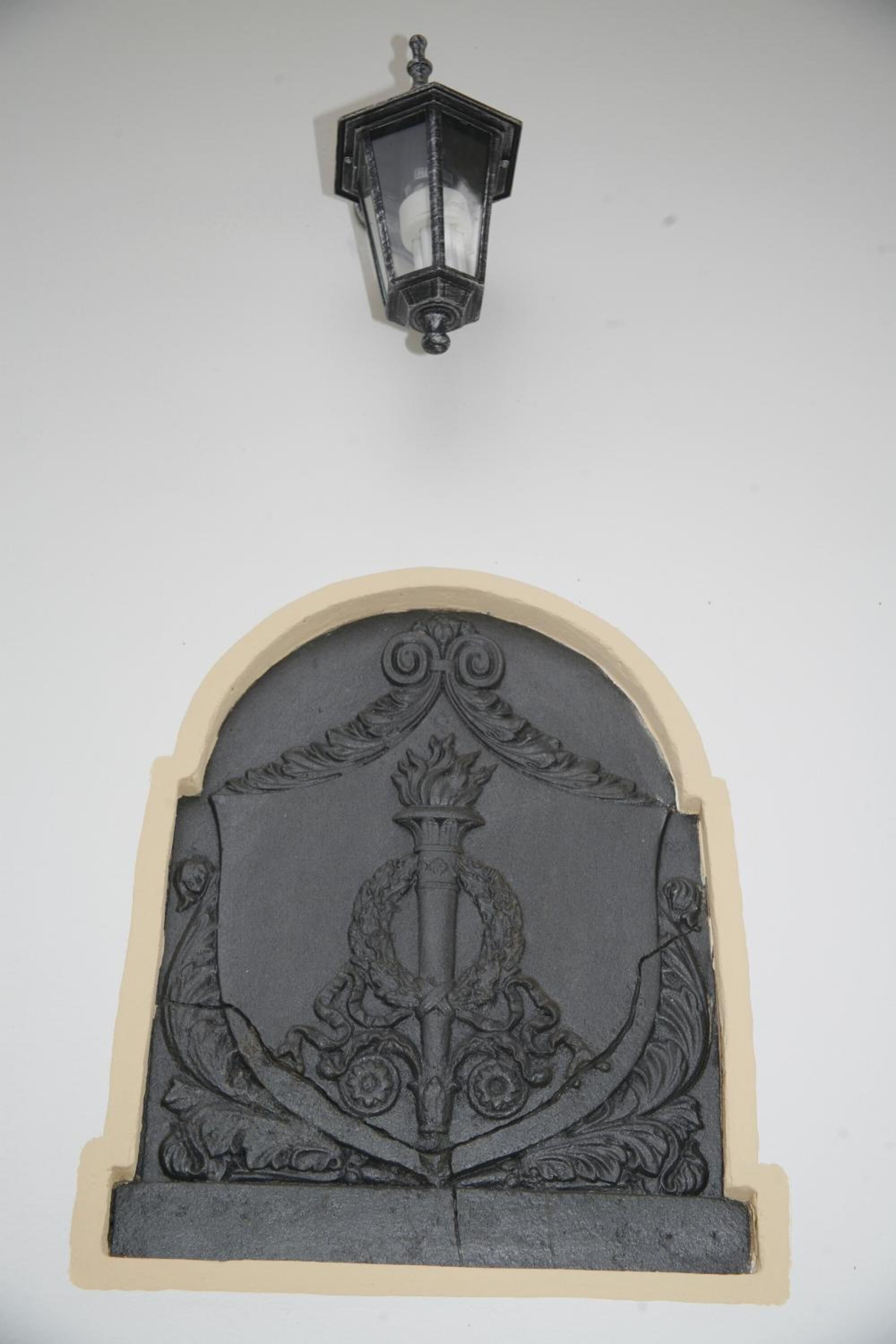 A wall-mounted decorative panel with an ornate design, including a central figure and a lantern above it.