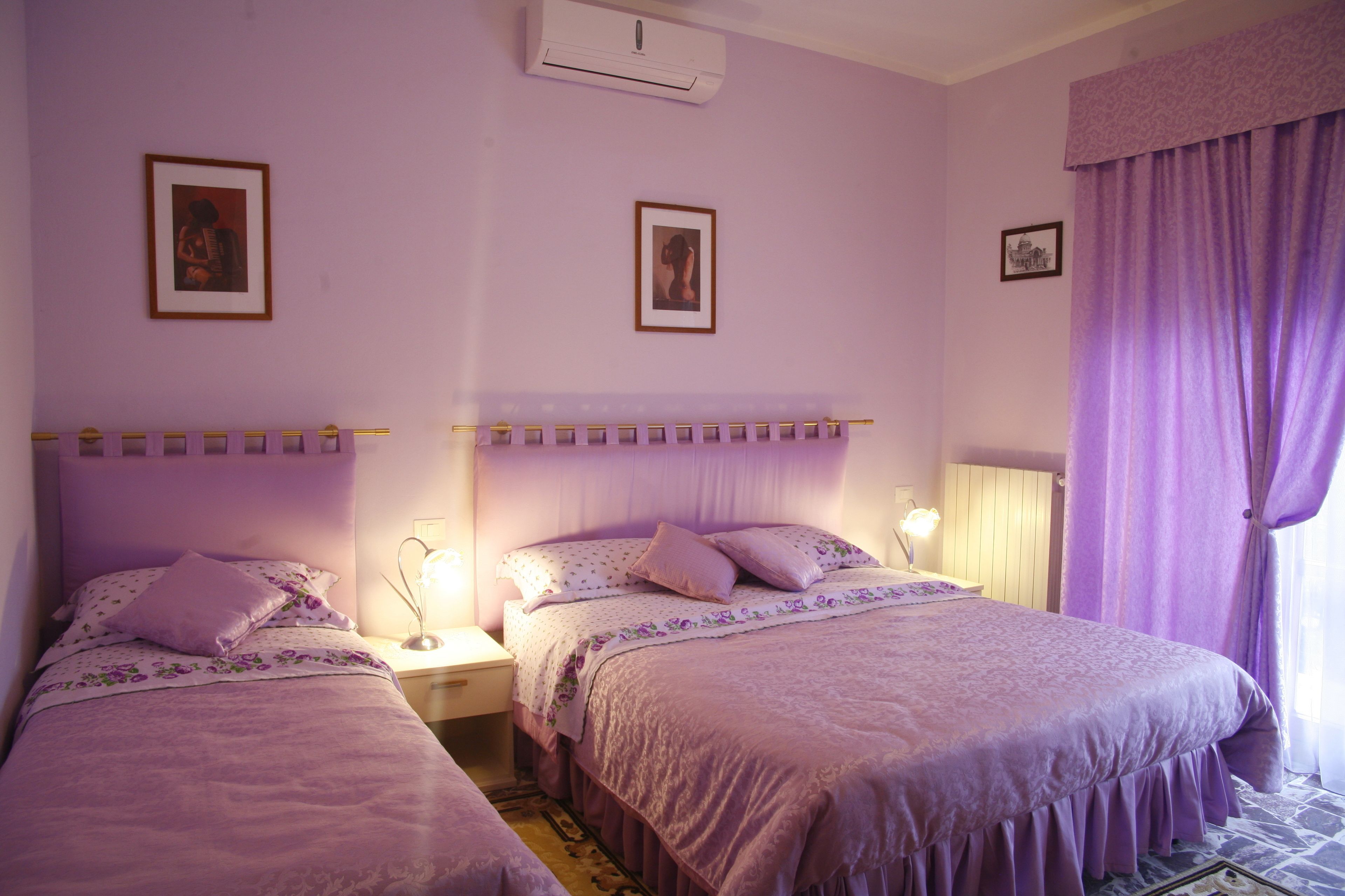 A room with two beds, each with a headboard, a nightstand, a lamp, and a framed picture on the wall.