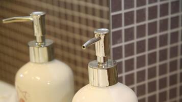 A bathroom with a white sink, two bottles of shower gel, and a hand towel.