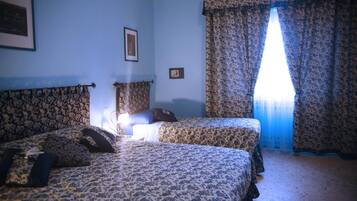 A room with two beds, floral-patterned bedding, a framed picture on the wall, and a window with patterned curtains.