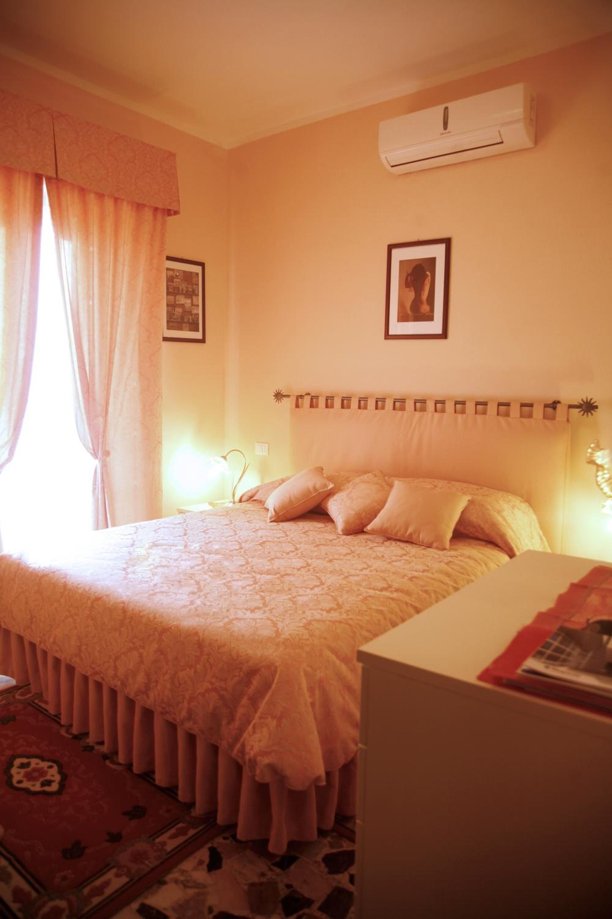 A bedroom with a large bed, a bedside table, an air conditioner, and a window with curtains.