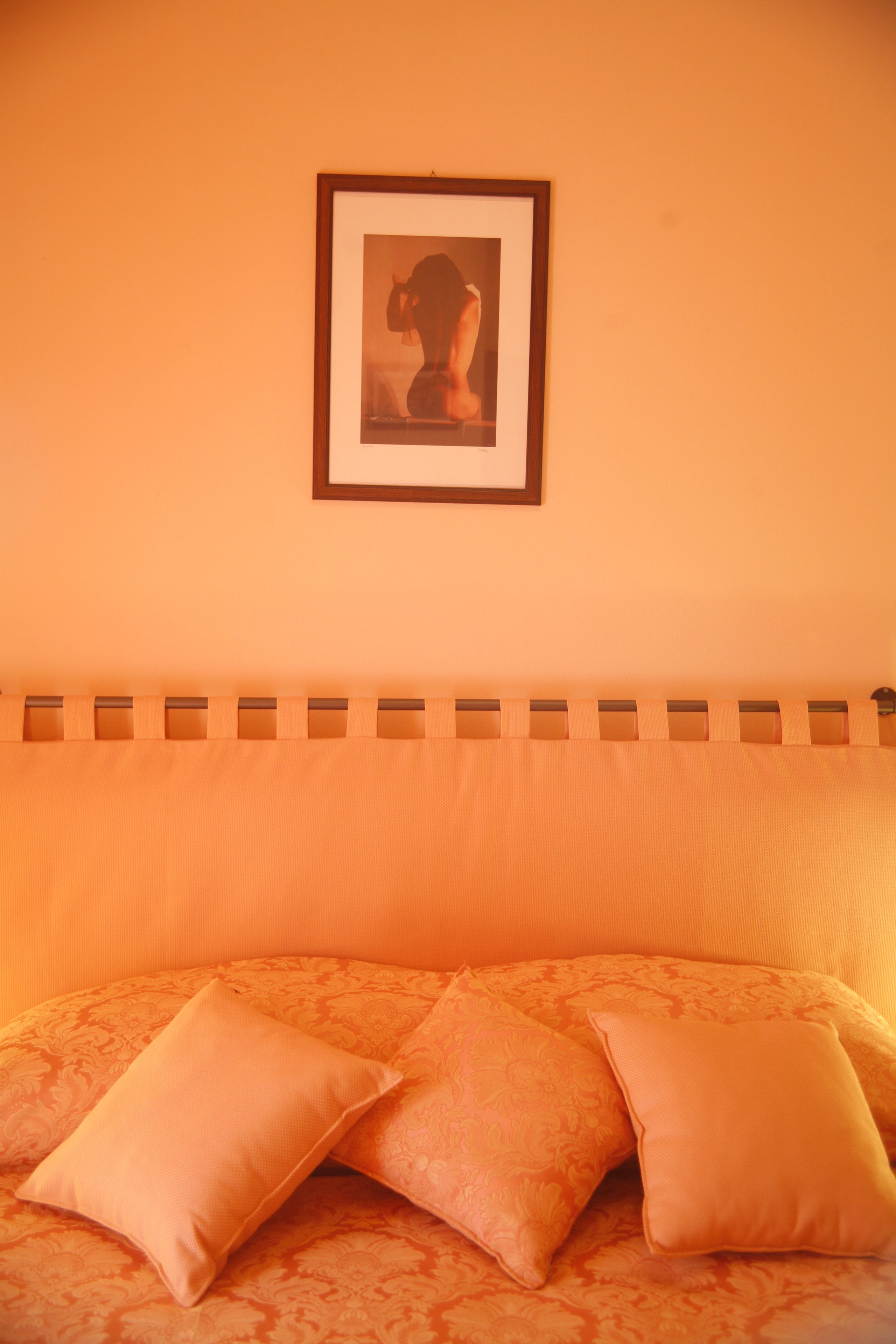 A bedroom with a bed, pillows, a headboard, and a framed picture on the wall.