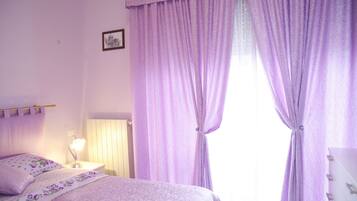 Une chambre à coucher avec un lit, une table de chevet, une lampe et une fenêtre ornée de rideaux violets.