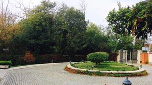 Un patio empedrado con un jardín circular central, rodeado de árboles y un muro de ladrillo.
