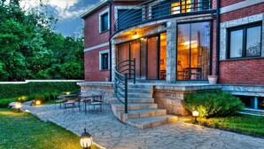 Una casa de ladrillo con un patio de piedra, mobiliario de exterior y una escalera que lleva a un balcón.