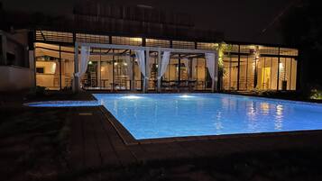Una piscina con plataforma de madera, rodeada por un espacio exterior cubierto con sillas y mesas.