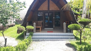 A building with a triangular roof, stone pillars, and a paved entrance. - Sandy Beach Bungalows (Gili Air)