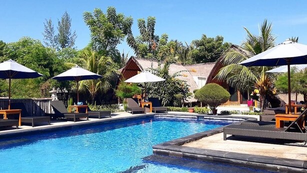A swimming pool with lounge chairs and umbrellas, surrounded by tropical vegetation and buildings. - Sandy Beach Bungalows (Gili Air)