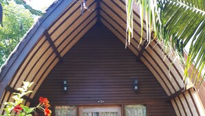 A wooden cabin with a pitched roof, a porch with wooden railings, and a red welcome mat. - Sandy Beach Bungalows (Gili Air)