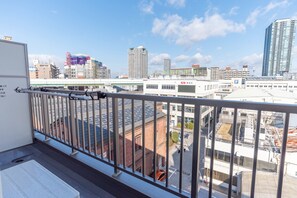 A balcony with a metal railing overlooking a cityscape with various buildings and a clear sky. - Villa Penthouse Tenma (Osaka)