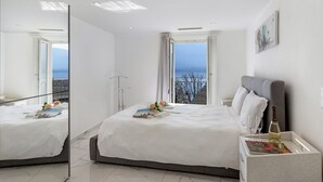 A modern hotel room with a large bed, a bedside table with a bottle and glasses, and a view of the sea through large windows. - Red View Apartment with Balcony Terrace, Ronco sopra Ascona, Switzerland (Ronco sopra Ascona)