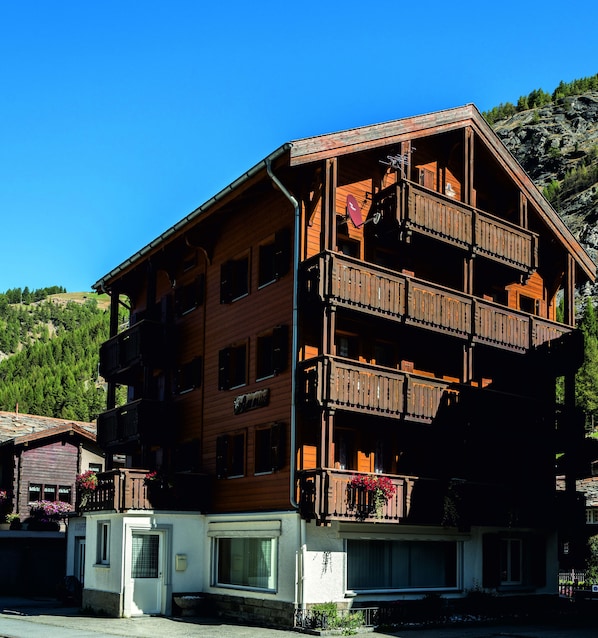 A multi-story wooden building with balconies, a visible ground floor entrance, and a sign indicating a restaurant.
