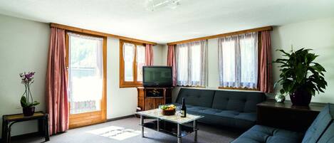 A living room with a sofa, a coffee table, a television, and a potted plant.