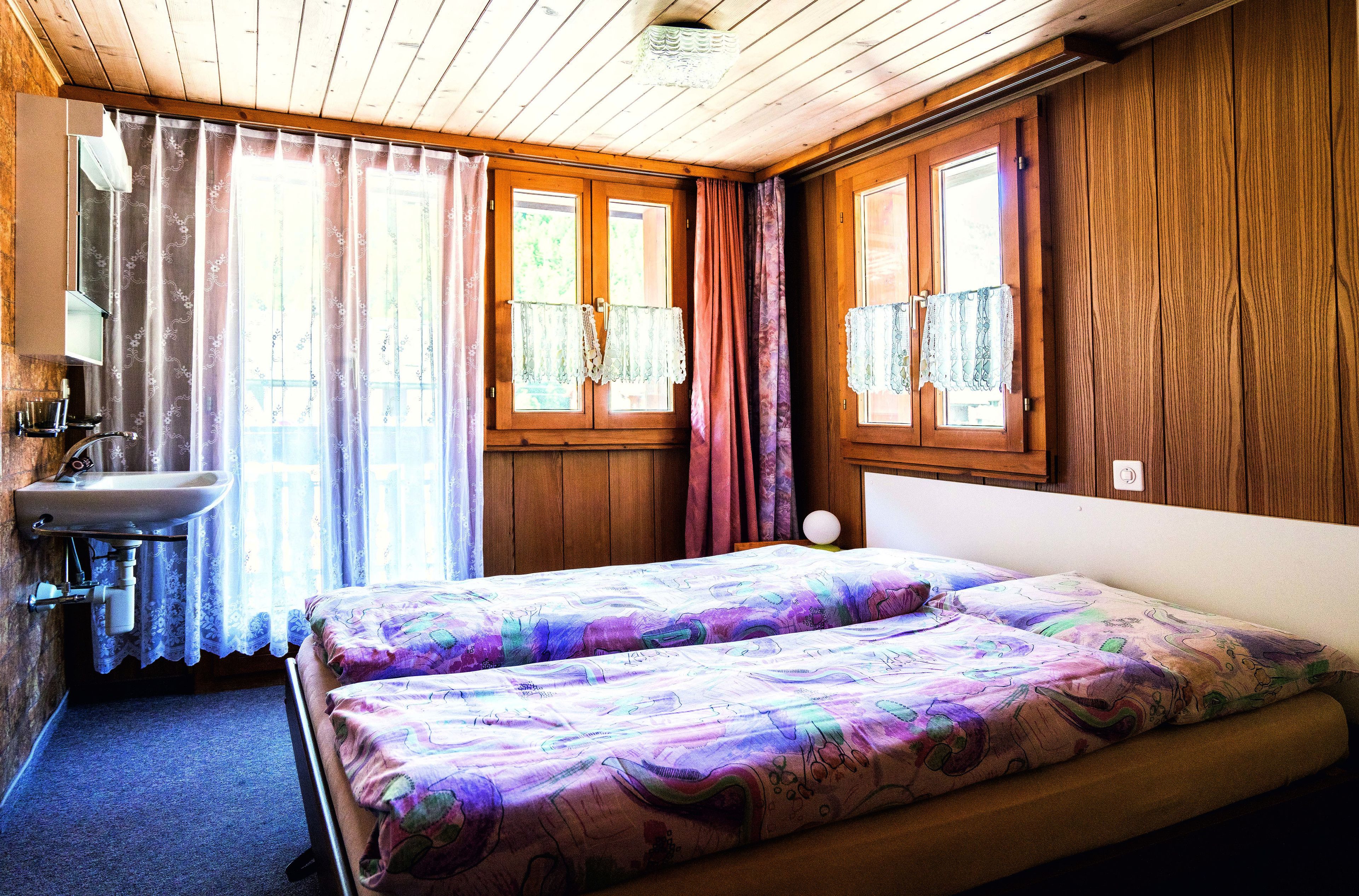 A room with wooden walls, a bed with floral bedding, a sink, and curtains.