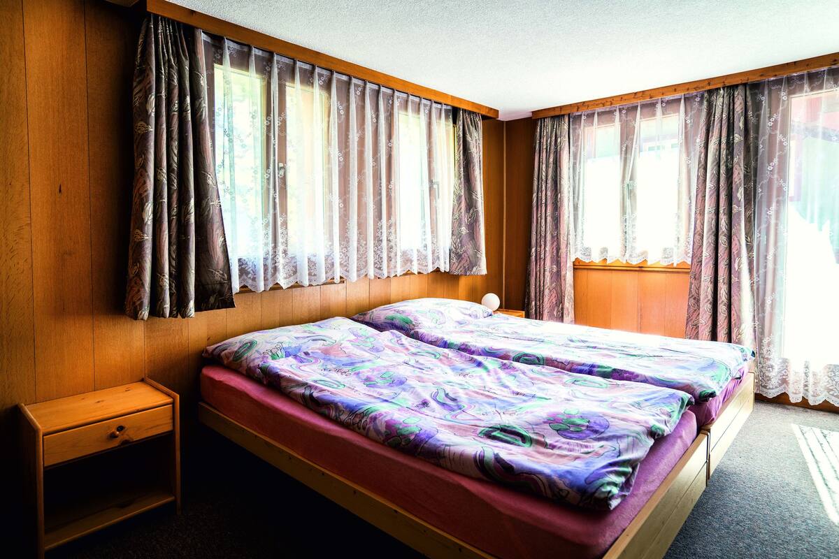 A room with a wooden bed, a nightstand, and a window with curtains.