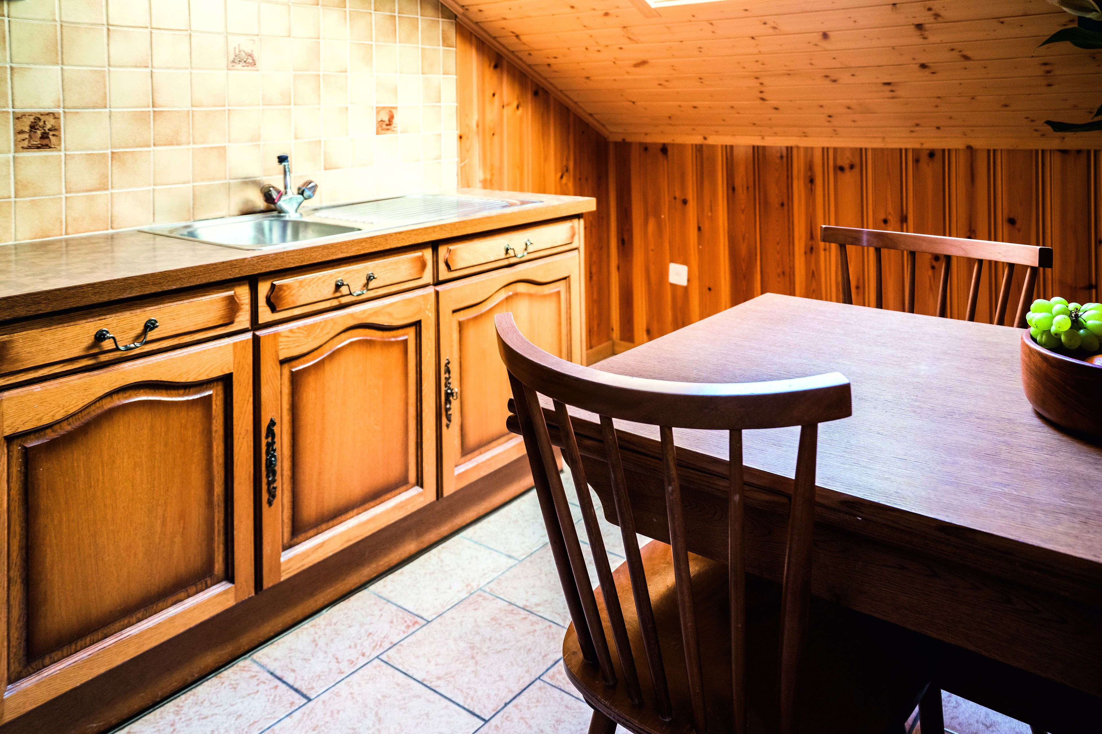 A wooden kitchen with a tiled backsplash, wooden cabinets, a sink, and a dining table with chairs.