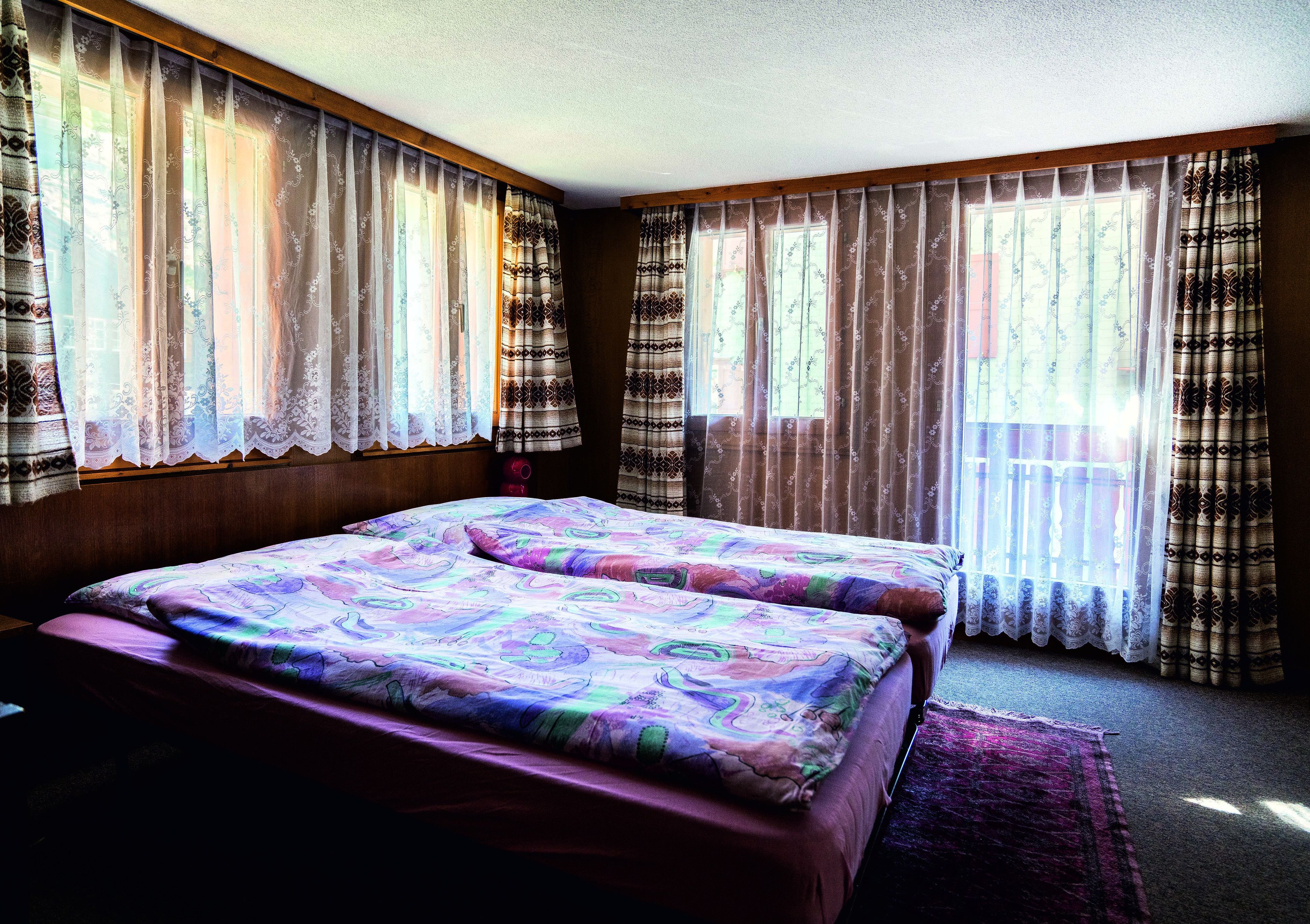 A bedroom with two beds, a wooden headboard, and a large window with patterned curtains.