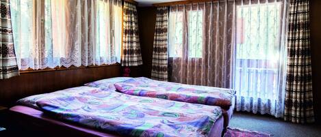 A bedroom with two beds, a wooden headboard, and a large window with patterned curtains.