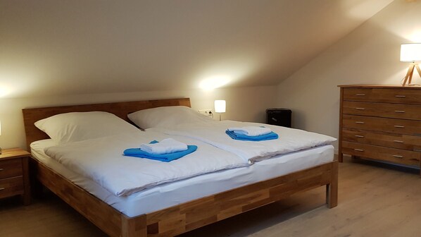 A single bed with a wooden frame and white bedding, a nightstand with a lamp, and a wooden dresser with drawers.