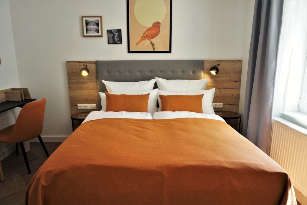 Une chambre d’hôtel avec un grand lit, deux tables de chevet, un bureau et une chaise. Chaque table de chevet est équipée de deux lampes fixées au mur.