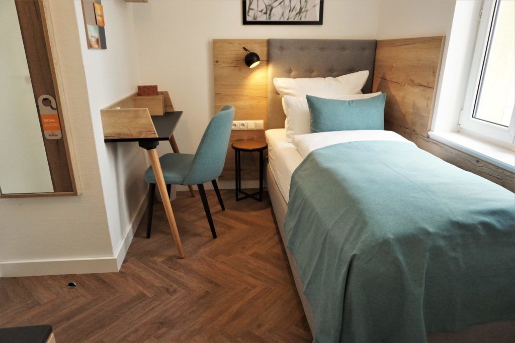 A bedroom with a bed, a desk, a chair, and a nightstand.