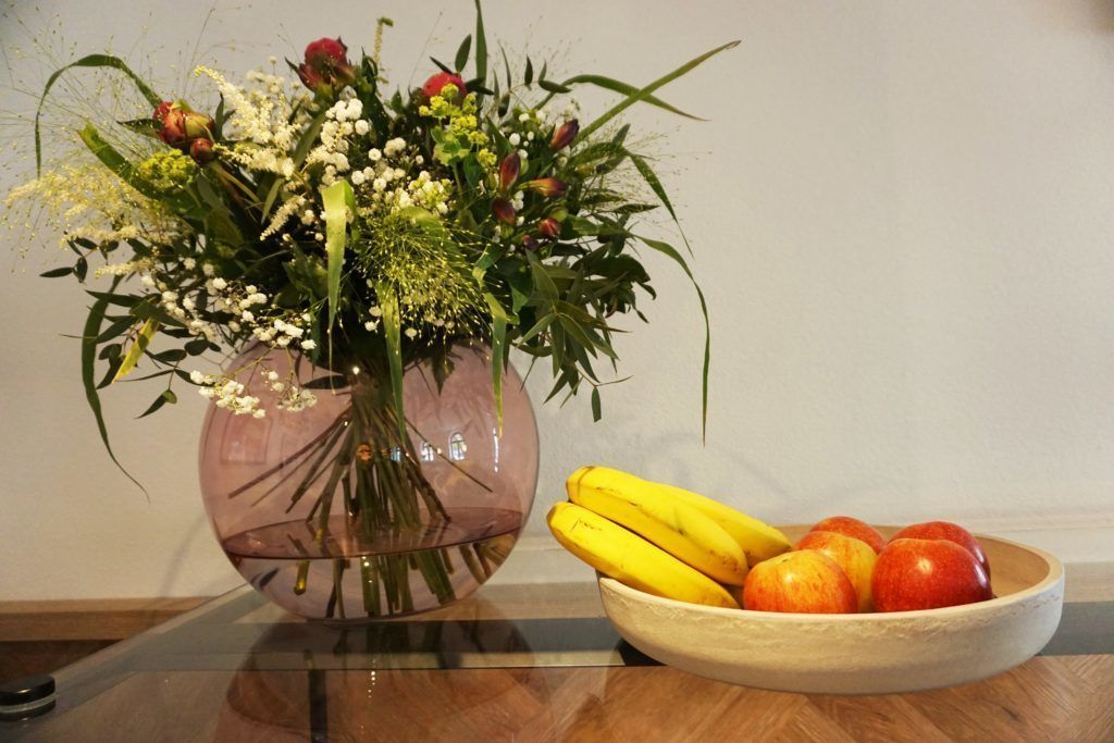A vase with flowers and a bowl of fruit on a table.