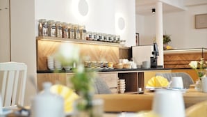 A modern cafe with a wooden counter, jars of condiments, and a seating area with tables and chairs. - dieSonne (Weimar)
