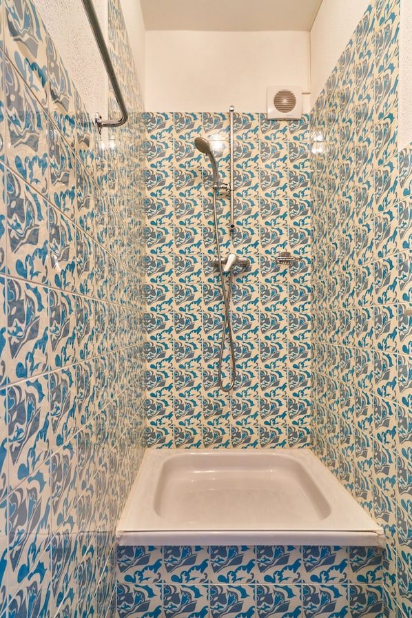 Un baño con ducha, paredes de azulejos y bañera.