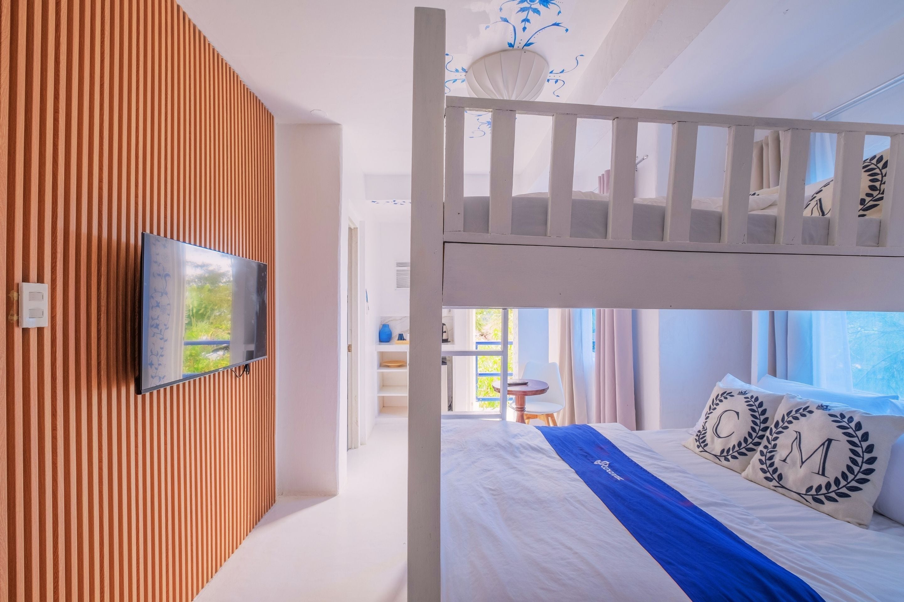 A modern hotel room with a bunk bed, a television mounted on a wooden wall, and a view of the outdoors.