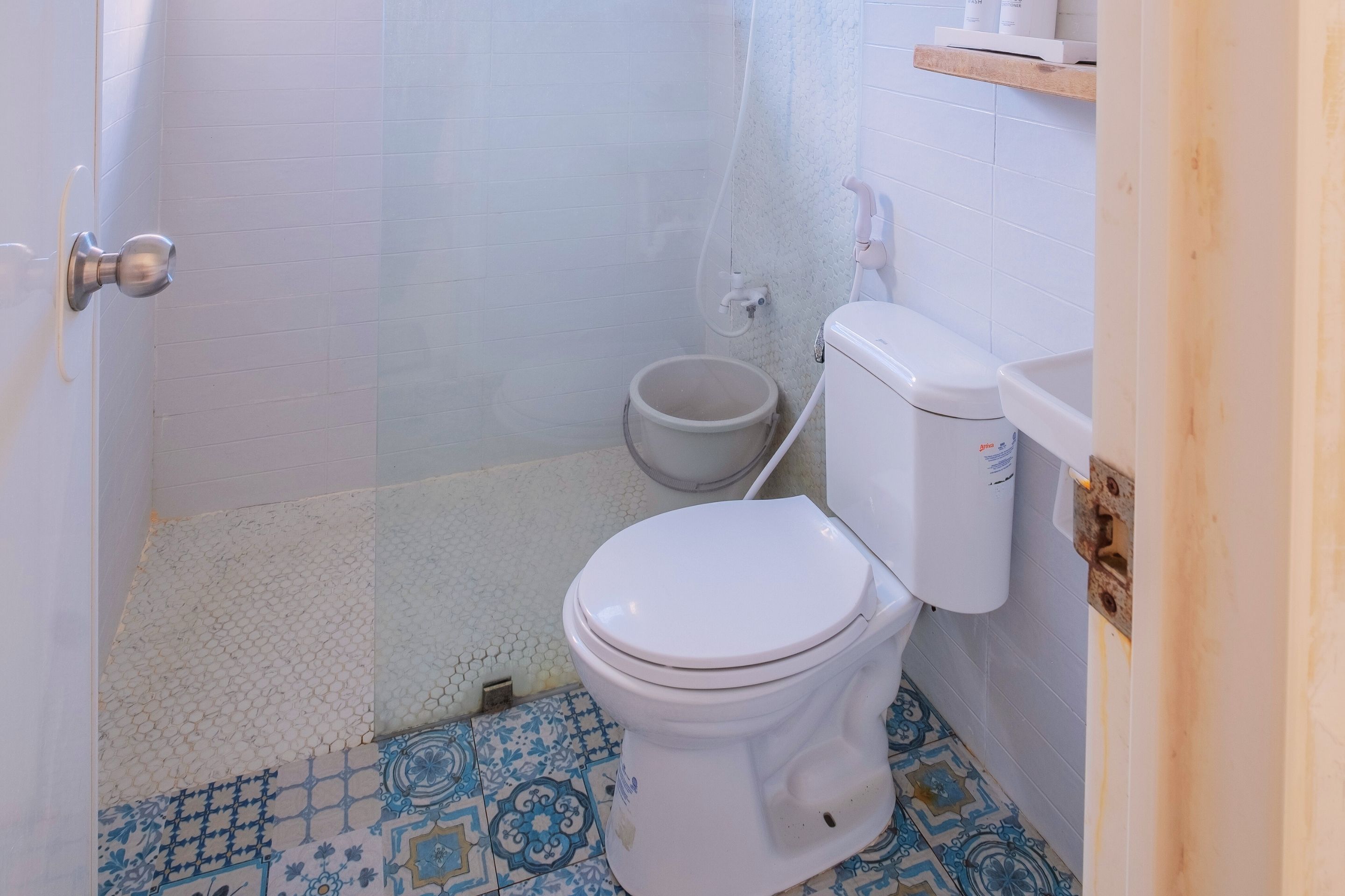 Une salle de bain avec des toilettes blanches, un espace douche et un carrelage au sol orné d’un motif bleu.