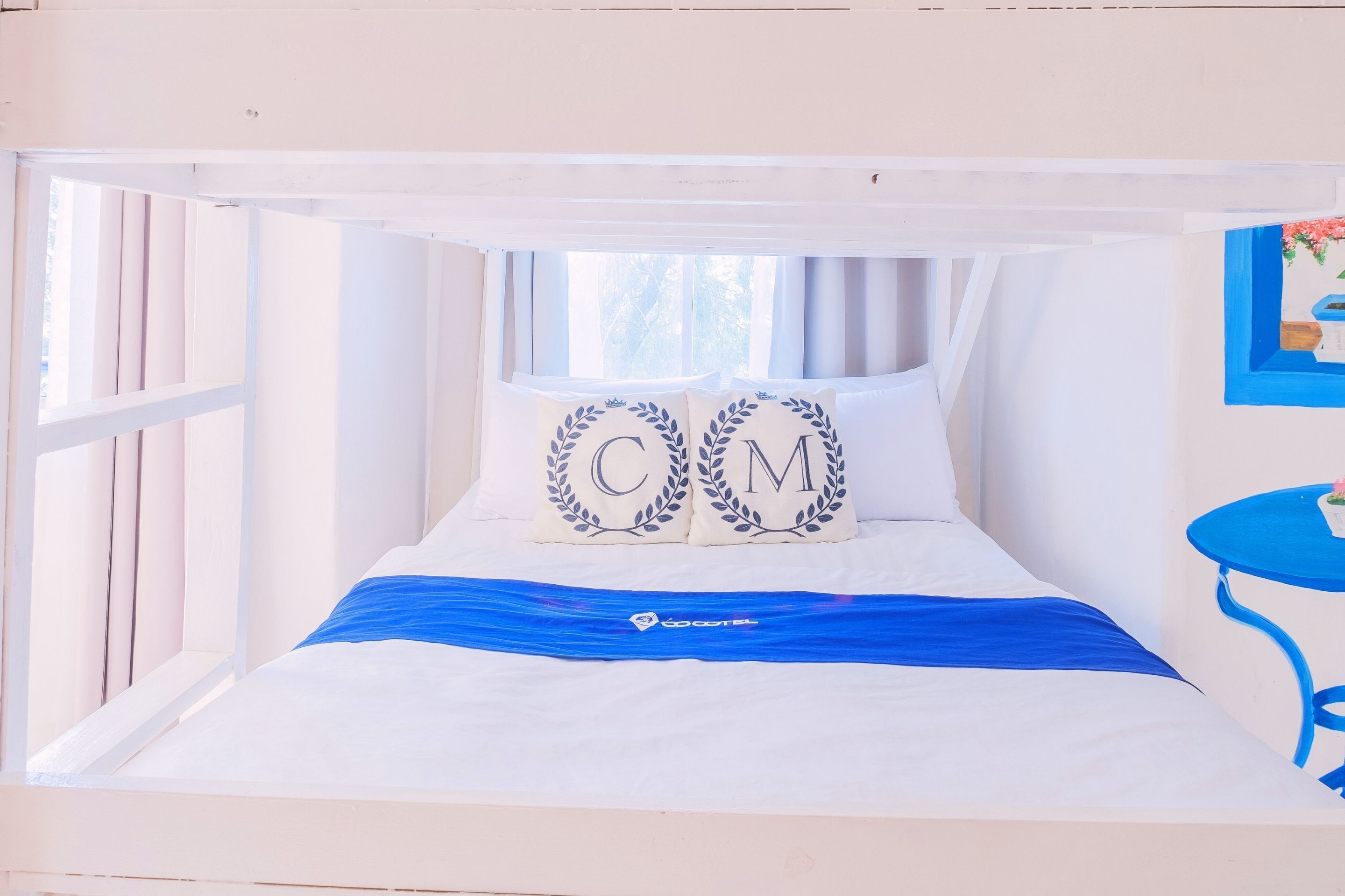 A bunk bed with two pillows featuring initials, a blue bedspread, and a small table with a plant.