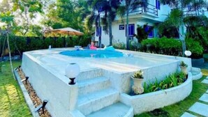 Una casa moderna de dos pisos con piscina, rodeada de exuberante vegetación y palmeras.