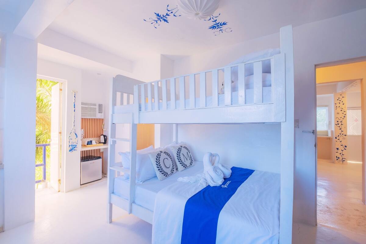Un lit superposé avec une literie blanche et des touches de bleu, une kitchenette et un balcon avec vue.