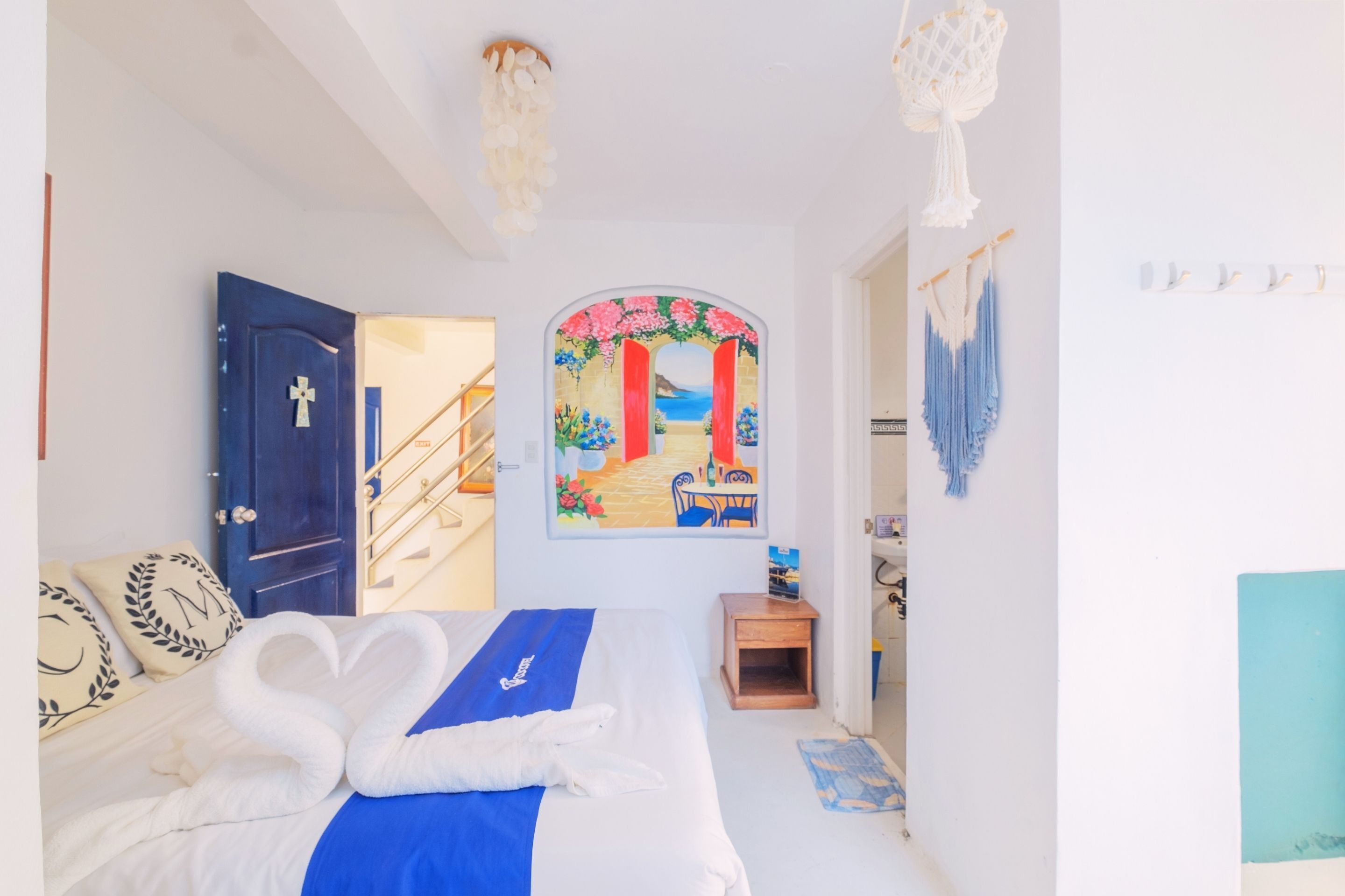 Un dormitorio con cama, una puerta, una escalera, un cuadro en la pared y un tapiz de macramé.