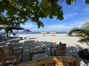 Un espace aménagé avec des chaises et des tables en bois, des parasols, situé en bord de plage et offrant une vue sur l’océan.
