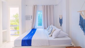 Un dormitorio con una cama grande, ropa de cama blanca, detalles en azul, una ventana con cortinas y decoración de macramé en la pared.